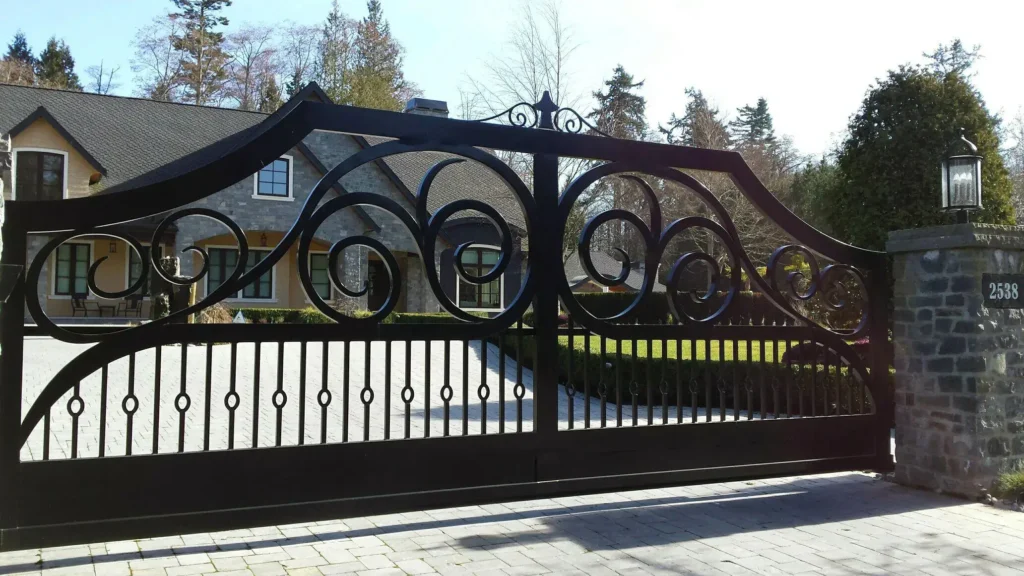 A grand black wrought iron gate with intricate swirls, securing a luxurious residence. Gates Wellington offers custom gate solutions—Contact Us for details