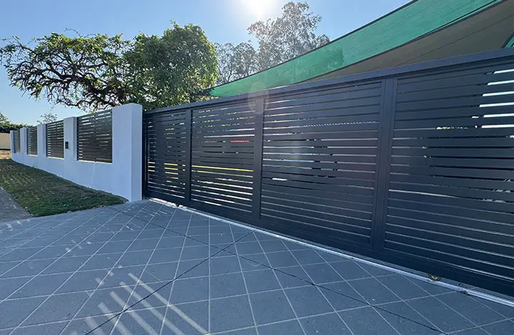 A modern black slatted aluminium gate providing privacy and airflow, seamlessly integrated with a white perimeter wall. Gates Wellington specializes in premium aluminium gates.