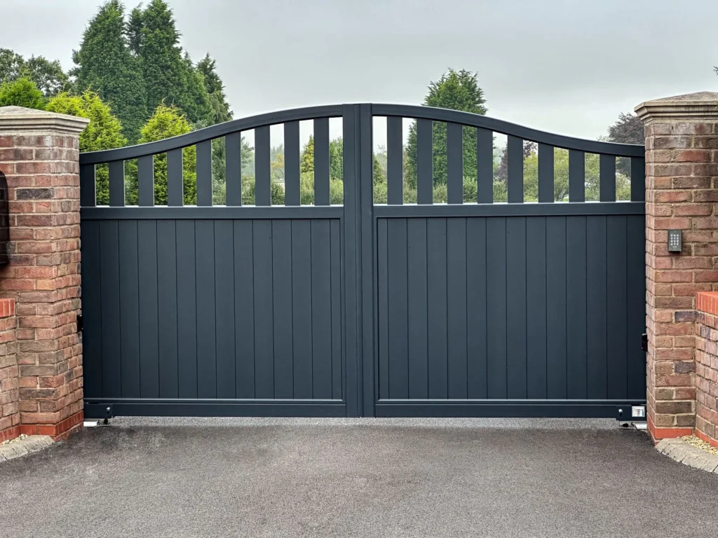 Modern black metal driveway gate with vertical slats and a curved top, enhancing security and aesthetics with Gates Wellington.