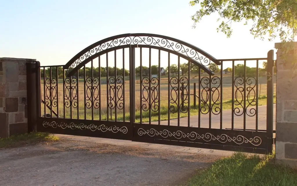 Ornate metal driveway gate at sunset, showcasing intricate scrollwork and elegance, provided by Gates Wellington. Learn more about us, our privacy policy, careers, newsletter, editorial guidelines, and terms and conditions to stay informed about our services and commitments.
